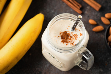 Wall Mural - Healthy banana cinnamon smoothie or shake in glass cup on dark background. Top view, selective focus