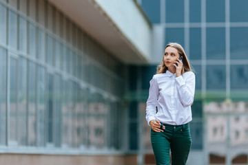 Young famale calling on a smartphone and walking on street. Attractive businesswoman talking by phone. Office building and in the Business District Background. Technology internet and happy people