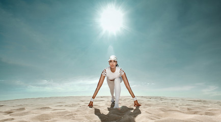 Wall Mural - Strong athletic woman sprinter, start running at the desert wearing in white sportswear. Fitness and sport motivation. Runner concept with copy space.