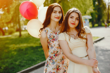 two young and bright girls spend their time in the summer park with balloons