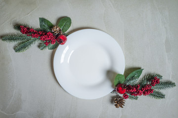 Empty plate dish with space for text and two decorative fir brunch on grey cement background. New Year and Christmas celebration traditional food concept.