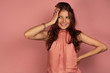 © bestsenny - The brunette stands on a pink background in a dress and in embarrassment holds her head with her hand.