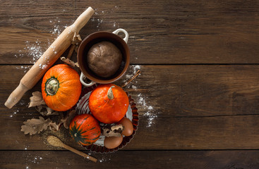 Poster - Raw pumpkin pie dough with dry autumn leaves, cane sugar, rolling pin and cinnamon sticks on wooden background with copy space