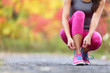 Autumn running shoes girl tying laces ready to run in forest foliage background. Sport runner woman training cardio in outdoor fall nature in pink activewear leggings and footwear.