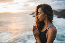 Young Woman Praying And Meditating Alone At Sunset With Beautiful Ocean And Mountain View. Self-analysis And Soul-searching. Spiritual And Emotional Concept