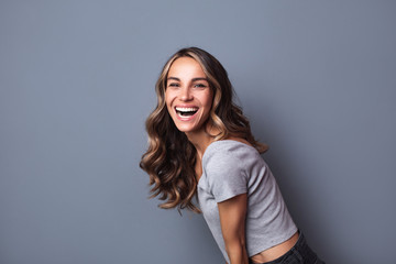 Wall Mural - Portrait of beautiful young girl laughing on grey background.