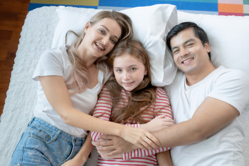 little girl smiling with mother and father on bed together in bedroom at home, young happy family concept