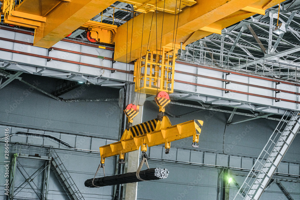 Yellow overhead crane carries cargo in engineering plant shop. Jib crab trolley with hooks and linear traverse. - obrazy, fototapety, plakaty 