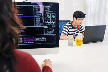 Wall Mural - concentrated asian teenager programming on laptop in office, his female colleague creating new softw