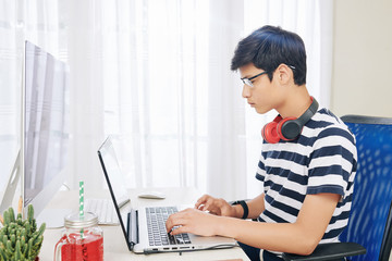 Wall Mural - serious mixed-race boy in glasses with headphones around his neck working on laptop in his room
