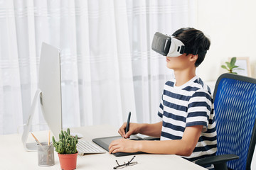 Wall Mural - teenage boy in virtual reality headset drawing on graphic tablet st his desk
