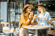 © rh2010 - Two female best friends spending time together on the cafe terrace, feeling happy standing with coffee and phone during a summer day