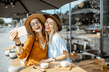 Two female best friends making selfie portrait while spending time together on the cafe terrace during a summer day