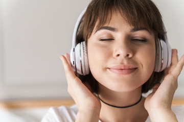 Relaxing young beautiful woman indoors at home listening music with headphones.