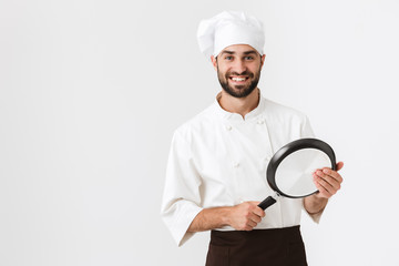 Wall Mural - Image of professional chief man in cook uniform smiling and holding frying pan