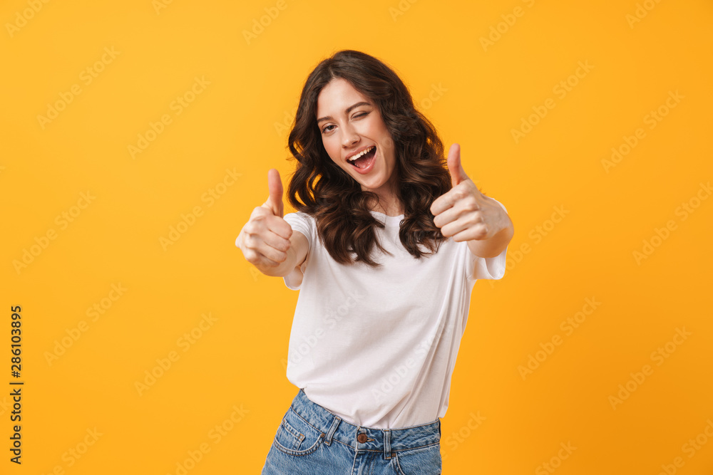 Image of beautiful brunette woman wearing casual clothes winking and showing thumbs up at camera - obrazy, fototapety, plakaty 