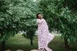 Beautiful dark skinned girl wrapped in sheet with fashion print posing at park with trees on background.