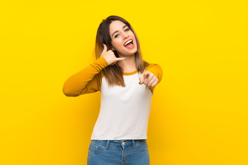 Wall Mural - Pretty young woman over isolated yellow wall making phone gesture and pointing front