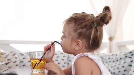 cute little girl drinks juice using drinking straw at the cafe on seashore. video shot of people on 