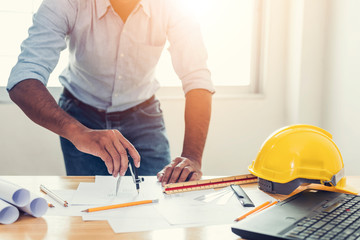 Asian architect man Standing working with blueprints sketching a construction project on wood desk at home office.Construction design concept.