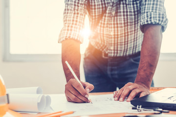 Asian architect man Standing working with blueprints sketching a construction project on wood desk at home office.Construction design concept.