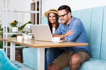 A couple sitting at cafe laughing cheerfully, looking at laptop screen