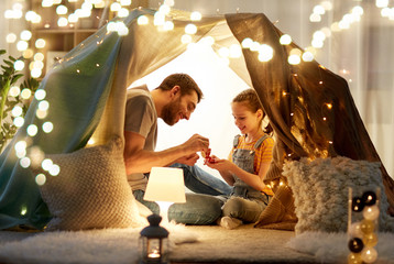 Poster - family, hygge and people concept - happy father and little daughter playing tea party in kids tent at night at home