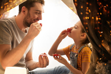 Wall Mural - family, hygge and people concept - happy father and little daughter playing tea party in kids tent at night at home