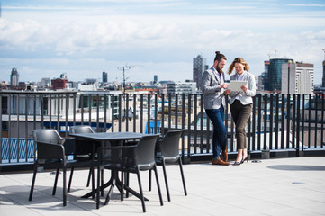 Wall Mural - Two young business people with tablet standing on a terrace outside office, working.