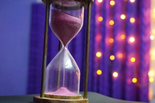 A Sand Clock With Light Purple Sand With Bokeh Background