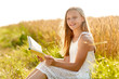 © Syda Productions - country, literature and leisure concept - smiling young girl in white dress reading book on cereal field in summer