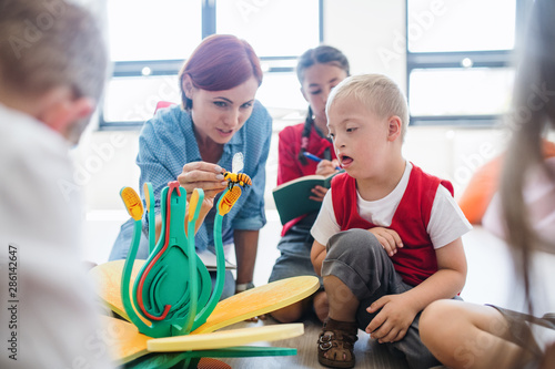 Fotomural A group of small school kids with teacher sitting on the floor in class, learning