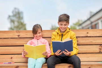 Wall Mural - education, childhood and people concept - happy school children or brother and sister reading books sitting on wooden street bench outdoors