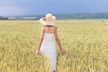 Beautiful Woman With White Dress And Hat Walking Away In Wheat Field
