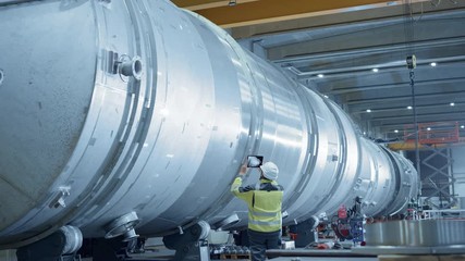 Wall Mural - Heavy Industry Engineer Uses Augmented Reality Digital Tablet to Scan Large Diameter Pipe. Modern Industrial Manufacturing Technology to Design and Construct Oil, Gas and Fuels Transport Pipeline.