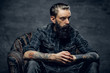 © Fxquadro - Bearded pensive man with tattooes is sitting on the armchair at dark room.