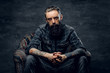 © Fxquadro - Bearded pensive man with tattooes is sitting on the armchair at dark room.