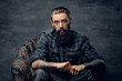 © Fxquadro - Bearded pensive man with tattooes is sitting on the armchair at dark room.