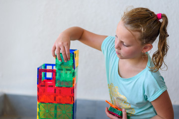 Beautiful teenage girl playing with lots of colorful plastic blocks constructor and builds house.