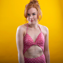 Cute Girl With Red Hair And Freckles Wearing A Pink Polka Dot Bikini With A Yellow Background