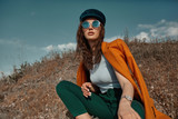 Fototapeta Tulipany - Autumn fashion. Beautiful attracrive young woman in bright autumn look. Orange trendy coat and pants and fashion sunglasses.