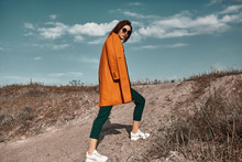 Autumn Fashion. Beautiful Attracrive Young Woman In Bright Autumn Look. Orange Trendy Coat And Pants And Fashion Sunglasses.