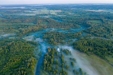 Wall Mural - Aerial view of the forest, field and river covered with layers of thick morning fog