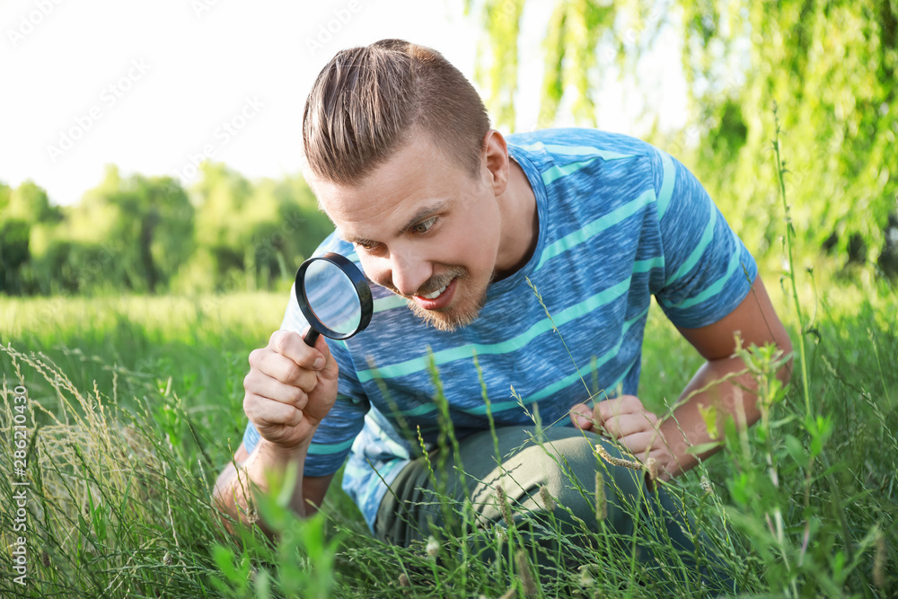 Young man with magnifying glass studying nature outdoors