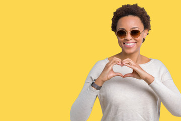 Beautiful young african american woman wearing sunglasses over isolated background smiling in love showing heart symbol and shape with hands. Romantic concept.