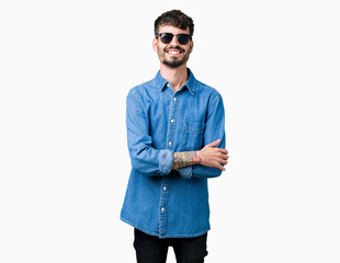 Young handsome man wearing sunglasses over isolated background happy face smiling with crossed arms looking at the camera. Positive person.