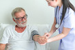 © Sasils Production - Senior man in bed with nurse in retirement home. Caucasian male with asian woman. Using blood pressure monitor.