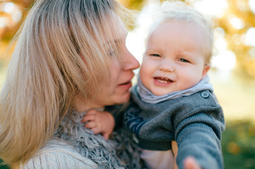 Wall Mural - Young smiling woman with her funny child closeup portrait at nature.