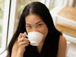© Phuttharak - Asian woman drinking coffee smiling and looking at the camera