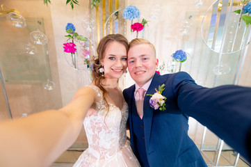 Funny wedding couple taking selfie on decorative wall background